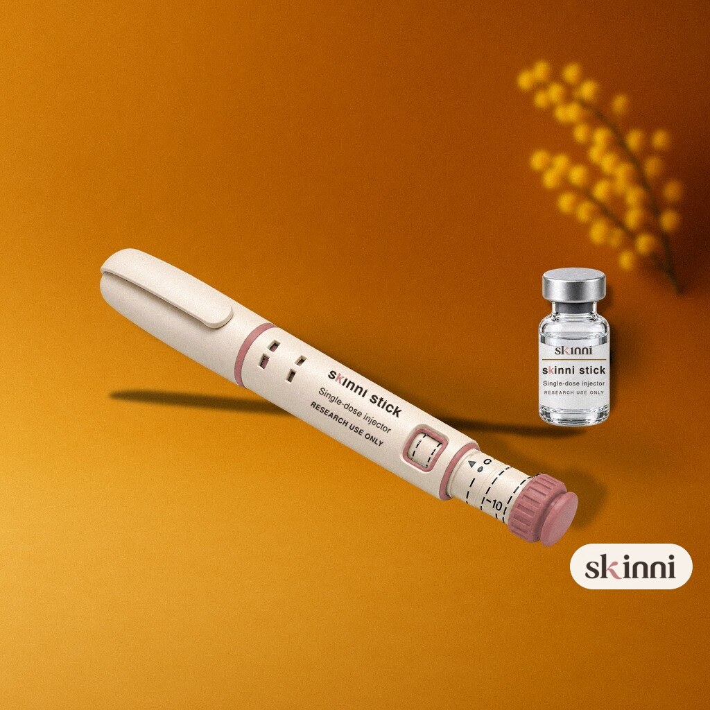 A clear Oxytocin research vial on a coloured plaster ledge, with botanicals beside it